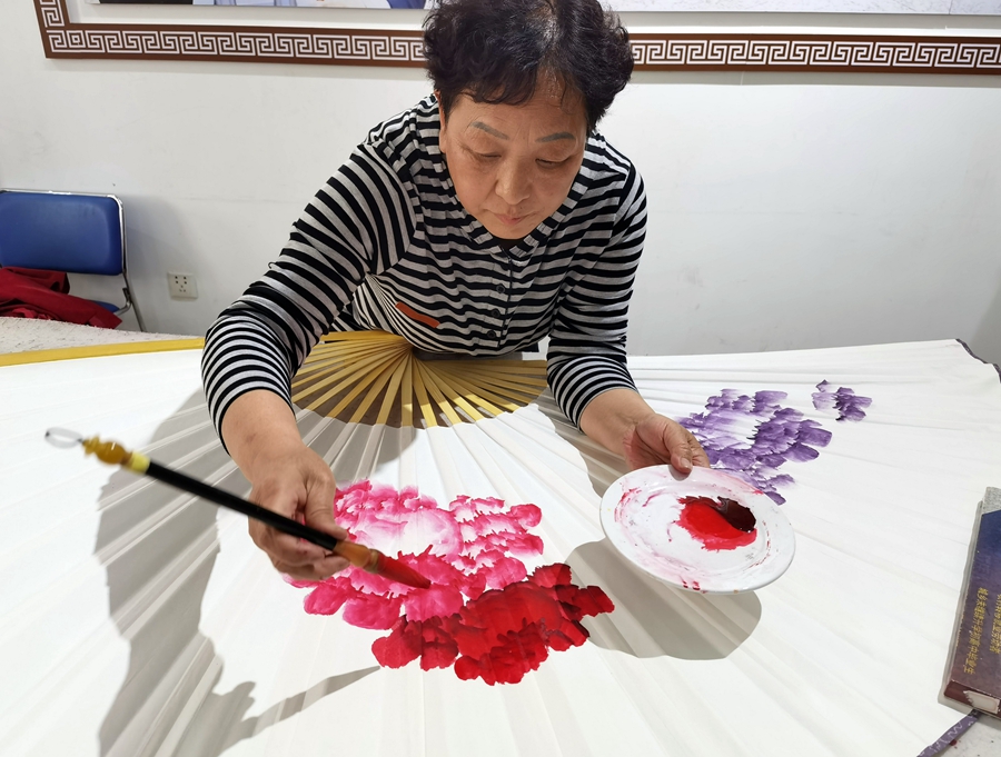 Seorang pelukis sedang mencipta lukisan peony pada kipas di komuniti Pingle, bandar Luoyang, pada 11 April 2023. (foto: Du Mingming/People.cn)