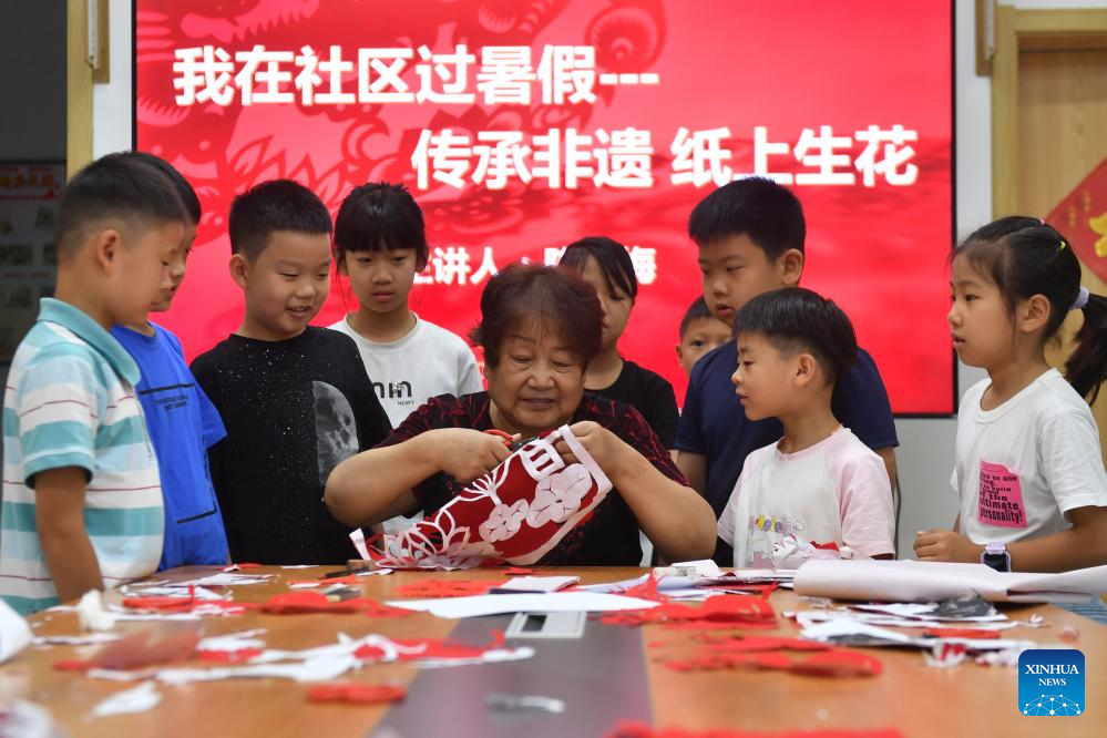 Seorang pewaris warisan budaya tidak ketara menunjukkan kemahiran seni guntingan kertas kepada kanak-kanak di Komuniti Jalan Barat Yinchuan, Daerah Shinan, Qingdao, Provinsi Shandong, timur China pada 22 Julai 2024. Ketika cuti sekolah musim panas pihak komuniti menganjurkan pelbagai aktiviti untuk mempelajari warisan budaya tidak ketara bagi memanfaatkan musim cuti sekolah para pelajar. (Xinhua/Wang Haibin)