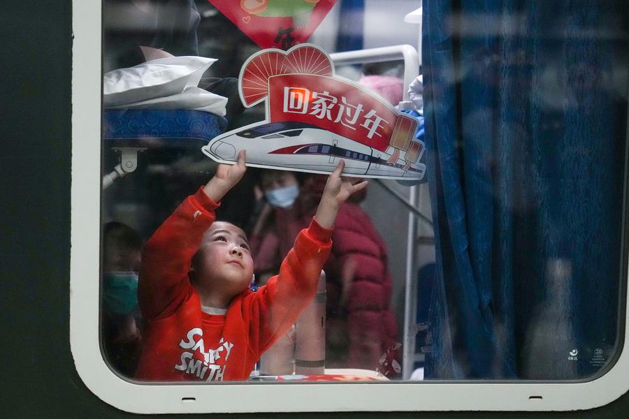 Seorang kanak-kanak memegang plakad yang berbunyi “balik kampung untuk Tahun Baru” ketika menaiki kereta api K4159, iaitu kereta api pertama yang berlepas dari Beijing di Stesen Kereta Api Barat Beijing pada 13 Januari 2025. (Xinhua/Ju Huanzhong)