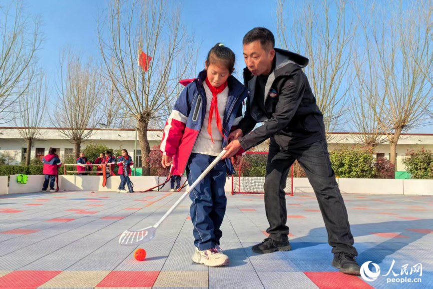 Bai Qingtao melatih seorang murid bermain floorball pada waktu rehat di padang Sekolah Rendah Sanhetou, pekan Chenqiao, kaunti Fengqiu di provinsi Henan, tengah China. (People's Daily Online/Cheng Minghui)