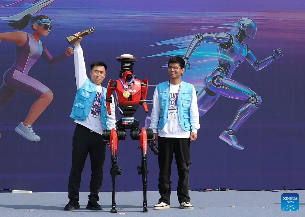 Pemenang pingat emas “Flash” (tengah) yang mewakili Pasukan Qitiandasheng dalam kategori berautonomi, bergaya pada upacara penyampaian pingat separuh maraton E-Town Beijing dan separuh maraton robot manusia di Kawasan Pembangunan Ekonomi-Teknologi Beijing di tenggara Beijing, China, 19 April 2026. (Xinhua/Zhang Chenlin)