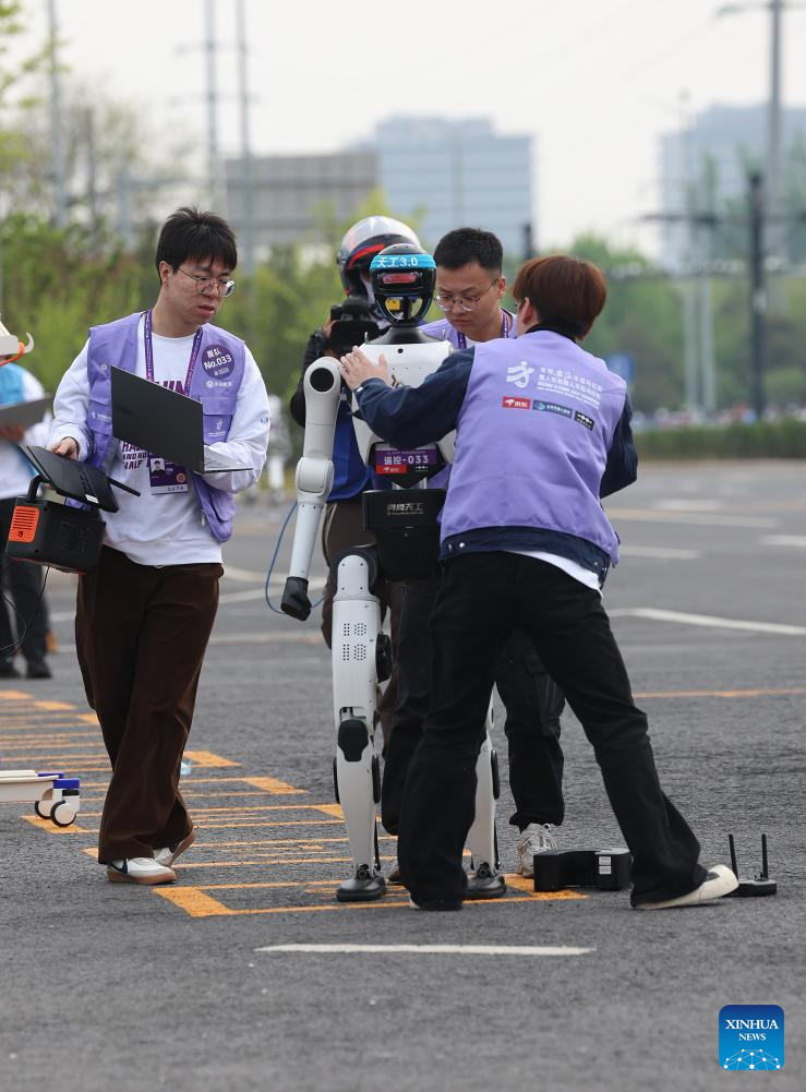 Jurutera memeriksa robot manusia "Tiangong 3.0" (kedua dari kiri) yang mewakili Pasukan Zhipaozhe dalam kategori kawalan jauh, pada separuh maraton E-Town Beijing dan separuh maraton robot manusia di Kawasan Pembangunan Ekonomi-Teknologi Beijing di tenggara Beijing, China, 19 April 2026. (Xinhua/Zhai Yifan)