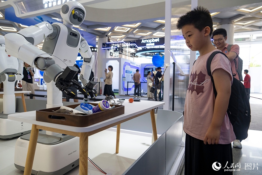 Seorang kanak-kanak terpesona melihat robot pintar mengenal pasti dan mengisih barang pada Persidangan Robot Dunia 2026 di Beijing, 19 Ogos 2026. (People's Daily Online/Weng Qiyu)