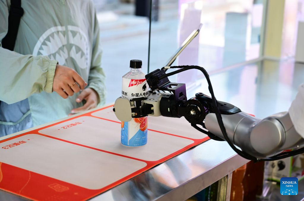 Sebuah robot mengambil sebotol minuman elektrolit dan memberikan kepada pelanggan di sebuah kedai robot pintar terkandung di Jalan Leijie, Hefei, provinsi Anhui, timur China, 26 Ogos 2026. (Xinhua/Zhou Mu)