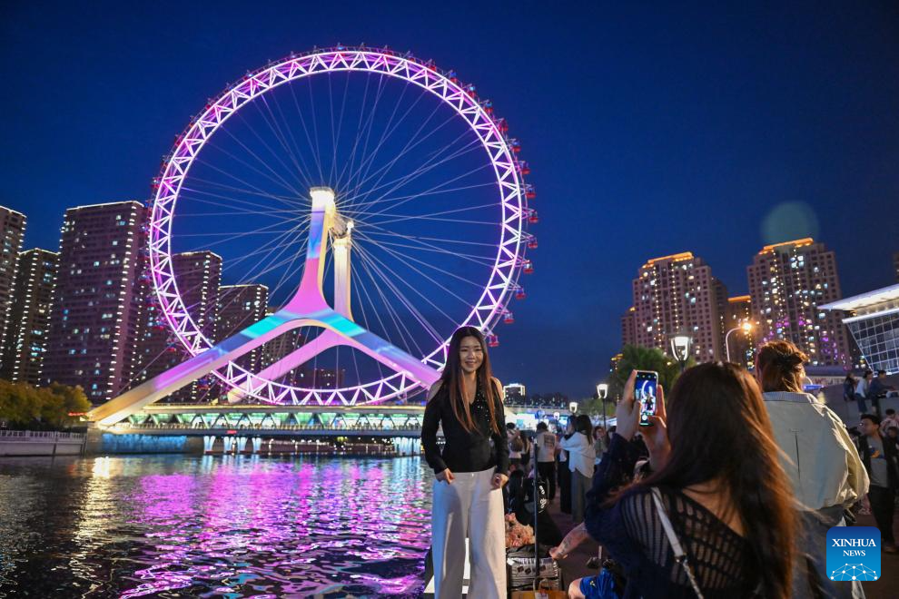 Seorang pelancong bergambar dengan roda Ferris “Tianjin Eye” di Tianjin, utara China, 24 April 2026. (Xinhua/Sun Fanyue)